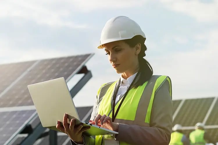 Woman in hard hat with laptop with solar panels