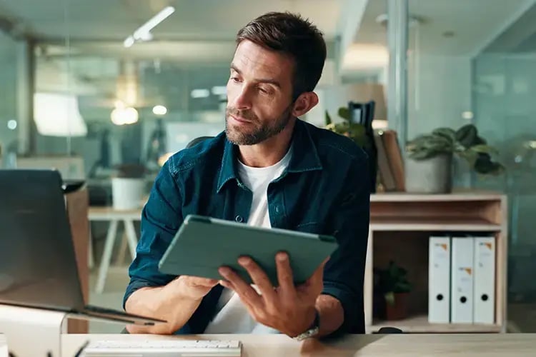 Man in office reading laptop and ipad