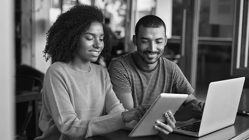 Two workers looking at ipad and laptop smiling